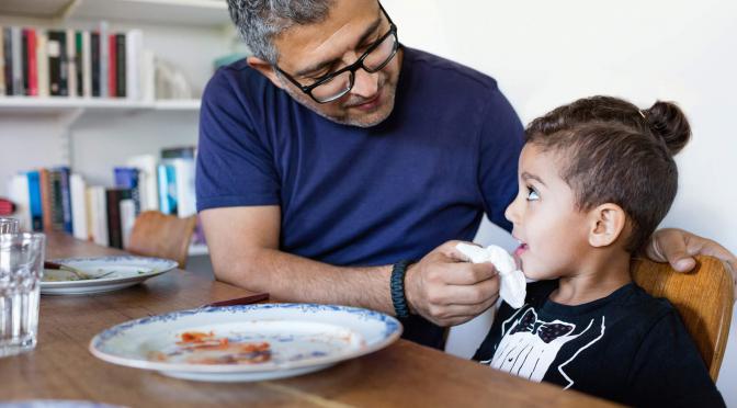 Parent wiping child's mouth at dining table.