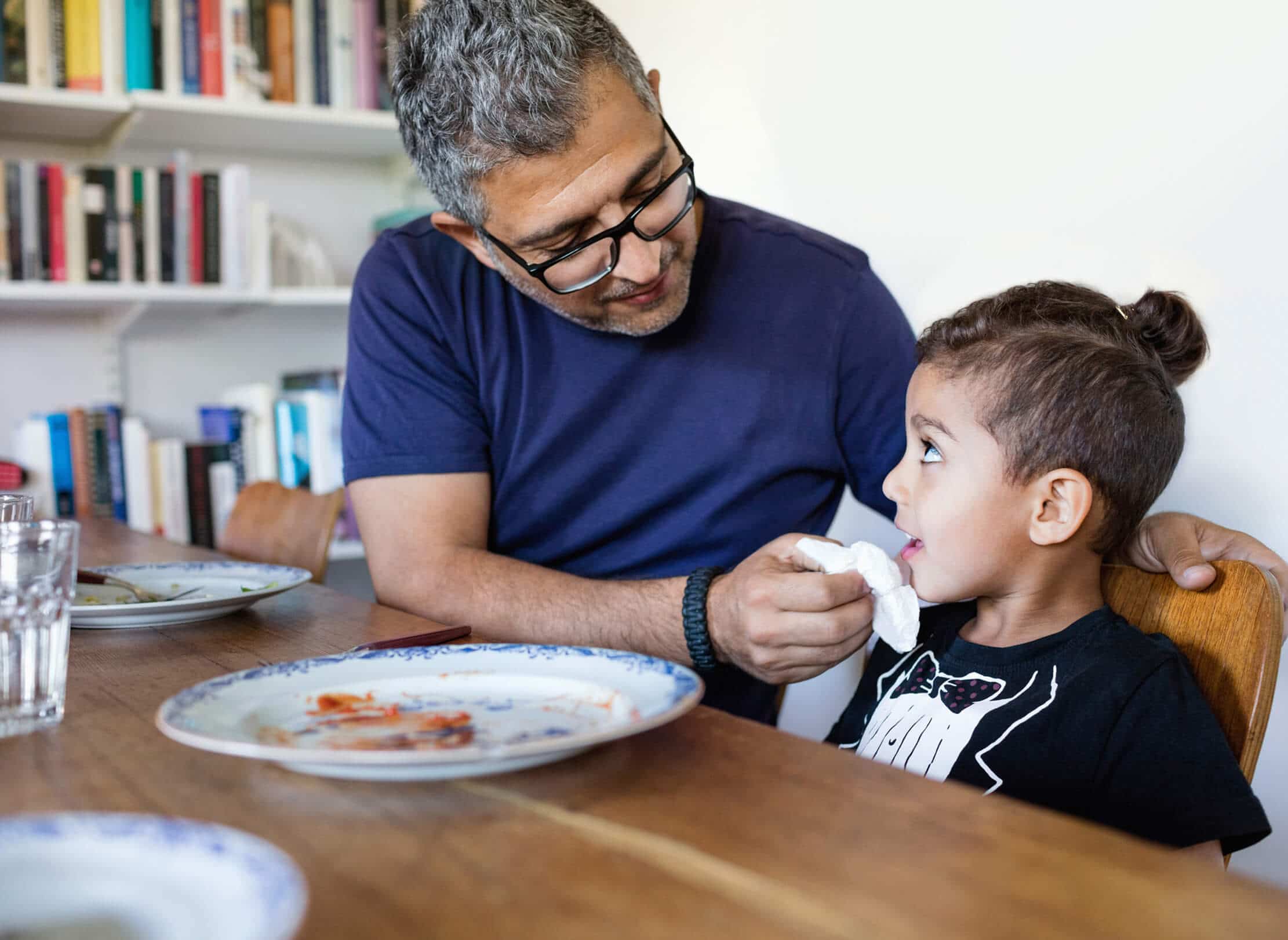 Parent wiping child's mouth at dining table.