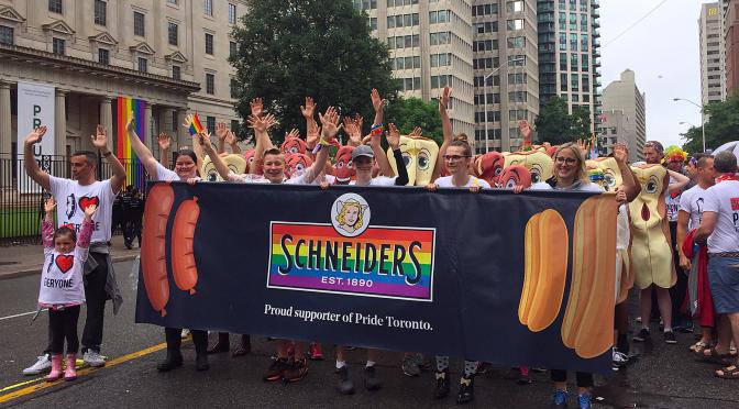 Employees marching in Pride Toronto parade holding Schneiders banner displaying pride colours.