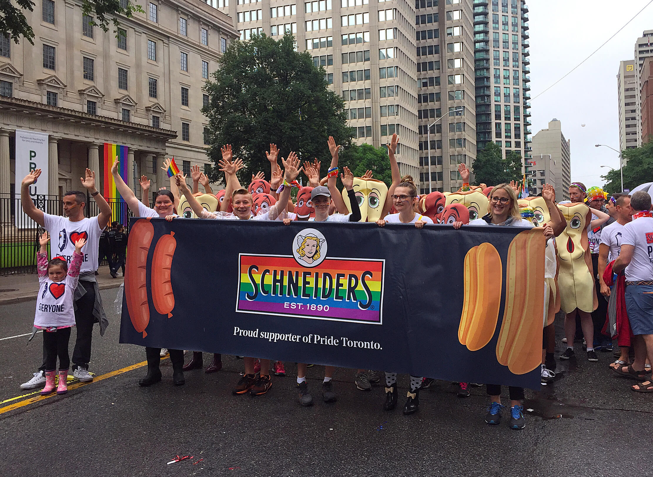 Employees marching in Pride Toronto parade holding Schneiders banner displaying pride colours.