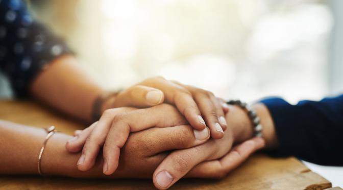 Closeup of two people holding hands in comfort.