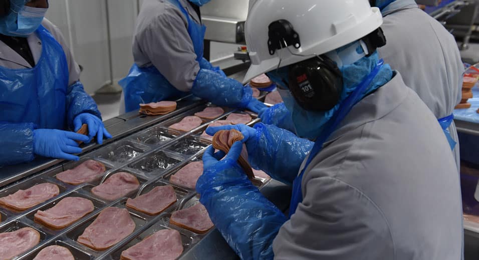 un membre de l'équipe emballe du jambon de charcuterie à l'usine Heritage