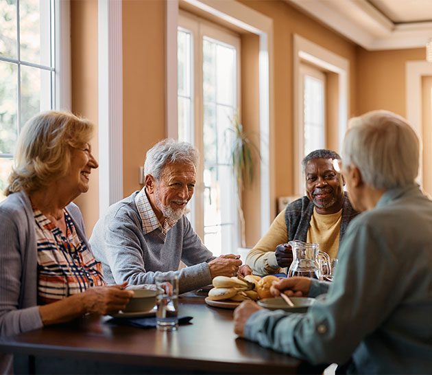 table avec quatre personnes âgées assises, souriantes et discutant