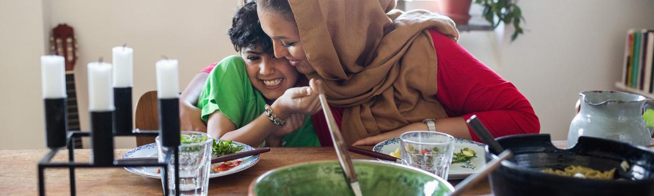 Woman hugging child at table during meal time.