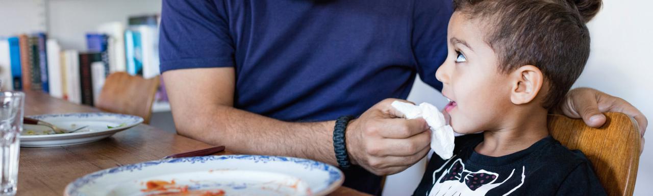 Parent wiping child's mouth at dining table.
