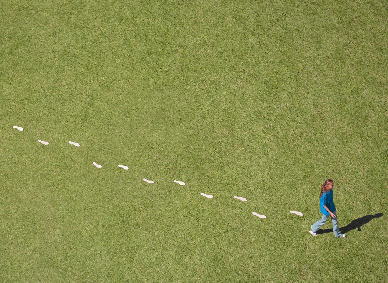 Woman walking on green grass with white footprints behind.