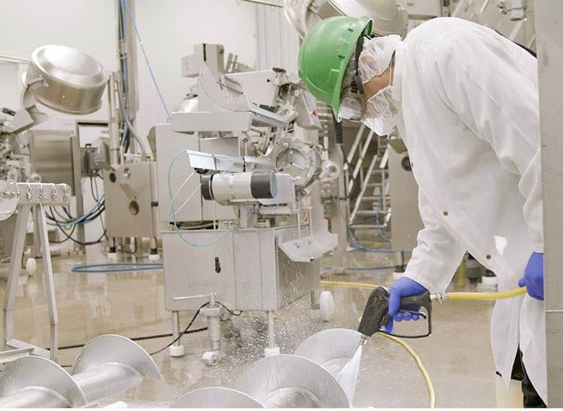 Employee using sanitation gun to clean plant machinery.