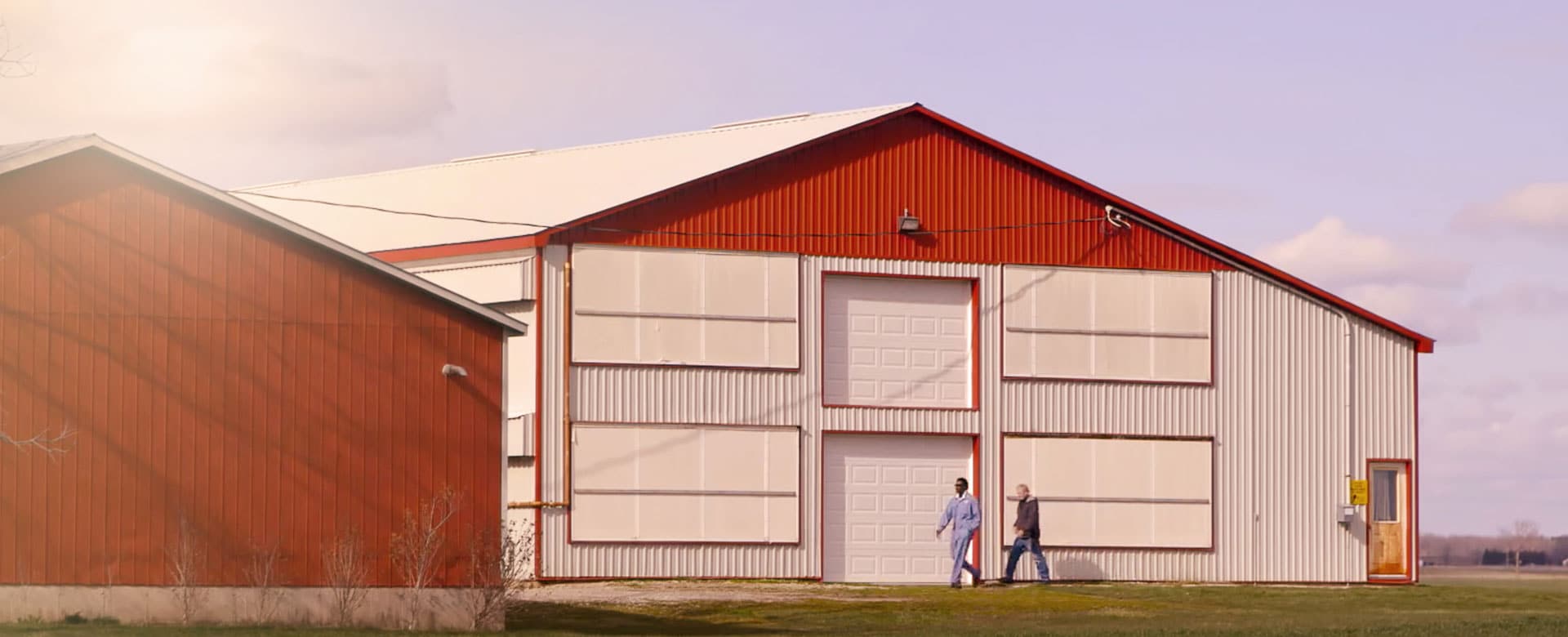 two men walking in front of red barn