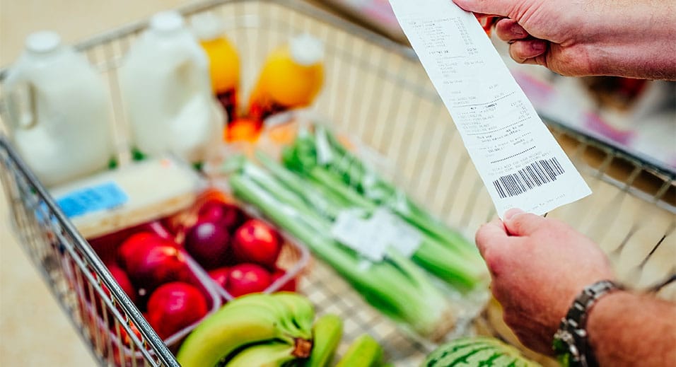 person in grocery store looking at receipt in front of grocery cart